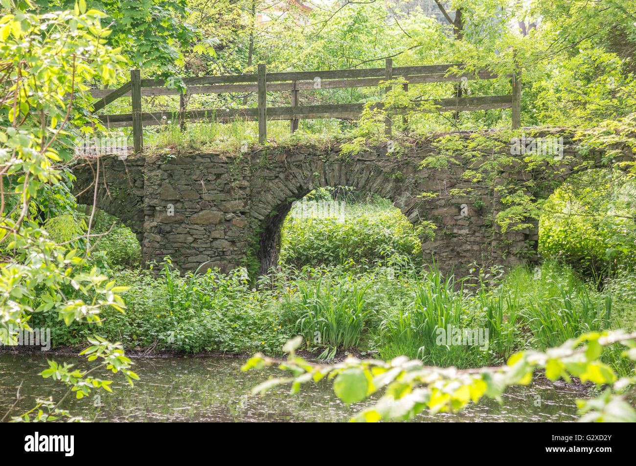 Ruined old stony bridge over the moat in the spring greenery Stock Photo