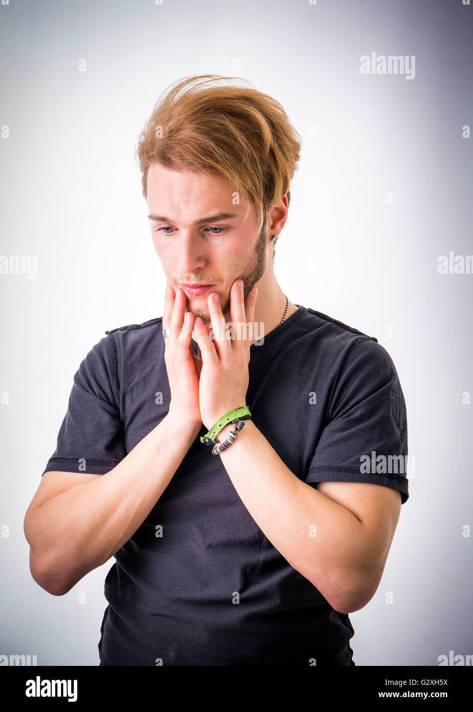 Sad or worried handsome young man looking down, on light background Stock Photo