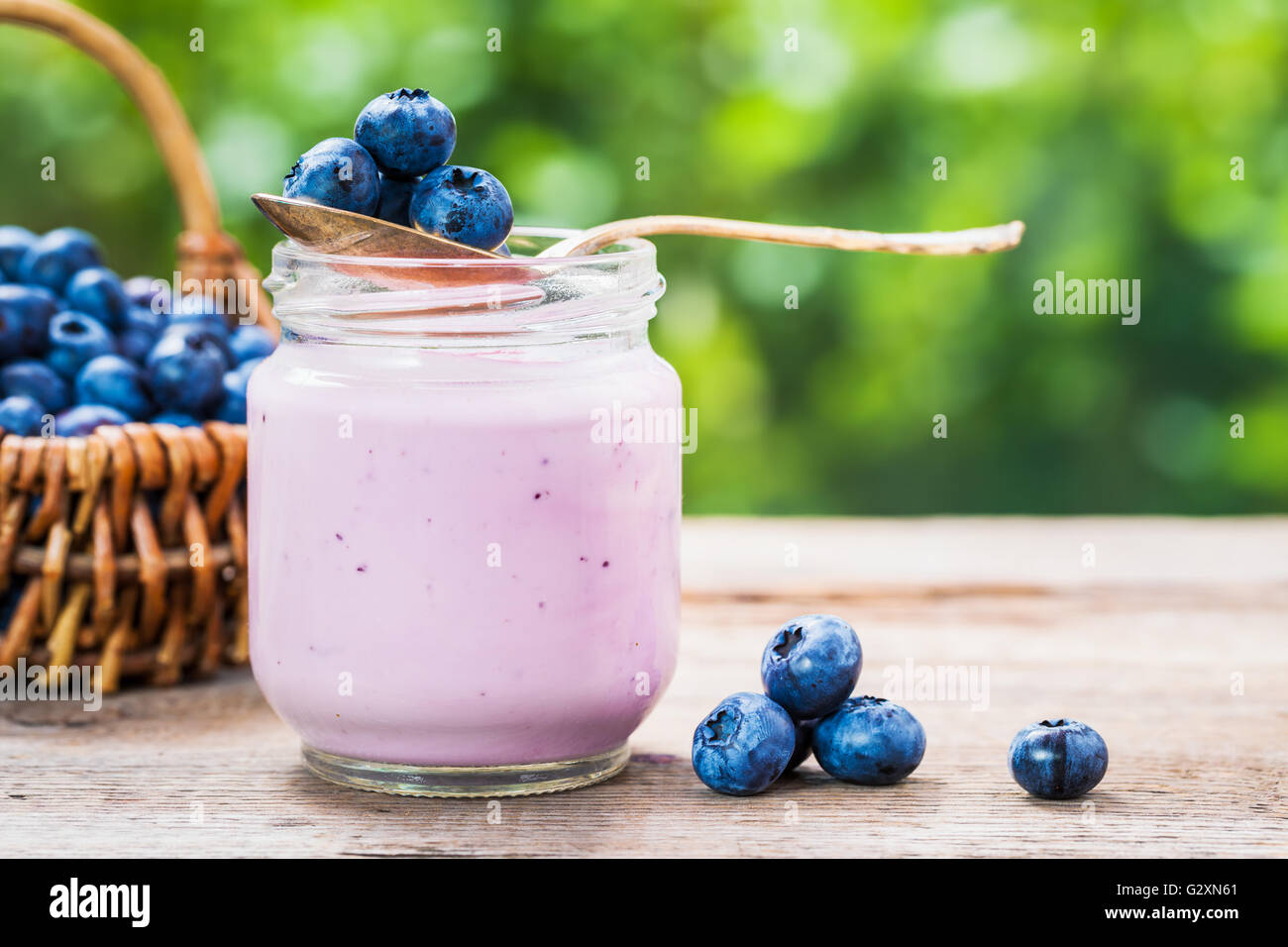 Blueberries yogurt in jar, basket of berries and saucer with bilberries on table outdoors. Stock Photo