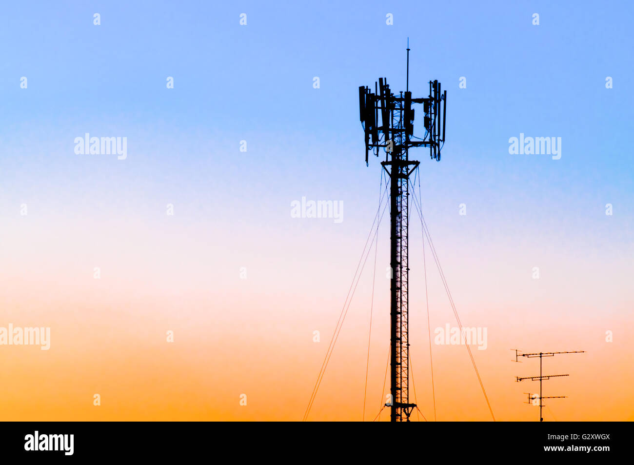 Silhouette of cellular tower against blue, pink and orange sunset sky. Also known as cell site or cell tower is where antennae a Stock Photo