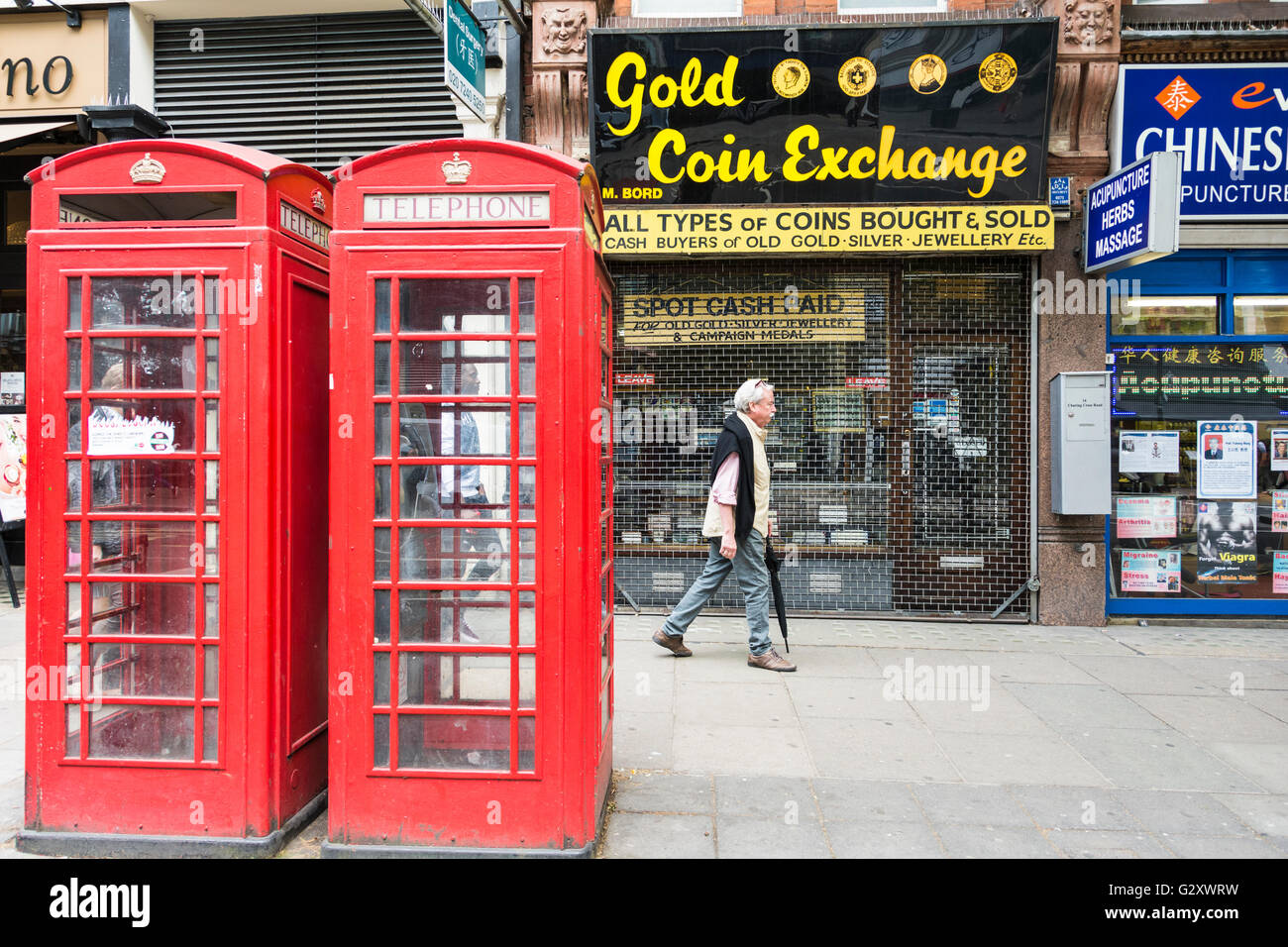 A  man passes the Gold Coin Exchange on Charring Cross Road next to two bright red K6 London telephone kiosks Stock Photo