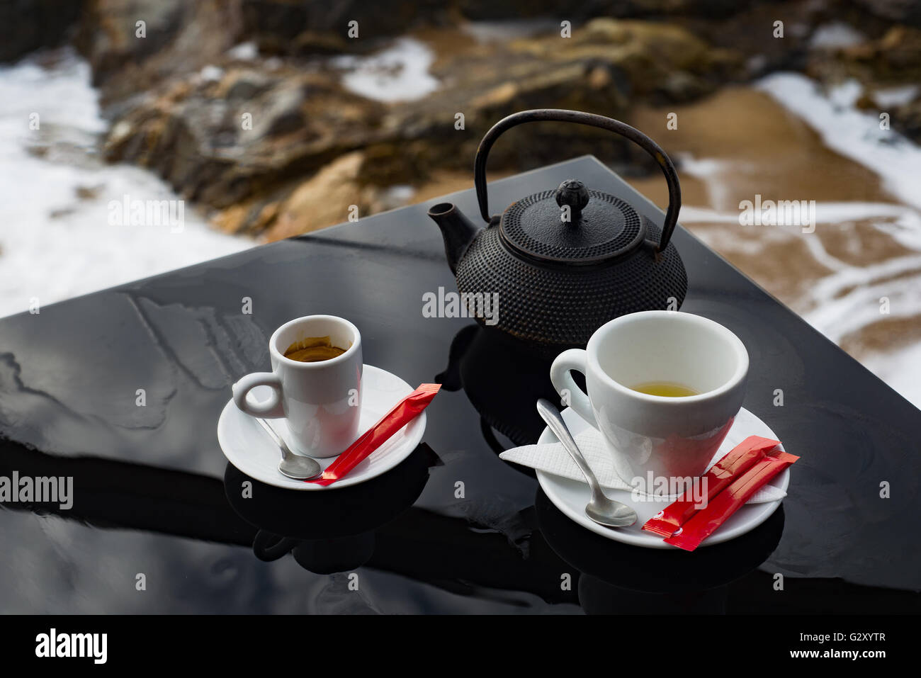 Tea and coffee cup pot set service on black shiny table with view of ocean shore Stock Photo