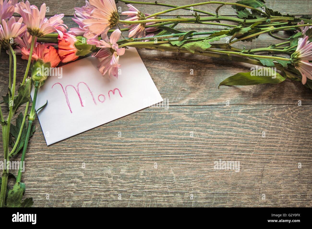 Gift For Mom. Flowers frame a handwritten card for Mom. Shot from above with rustic background and copy space. Stock Photo