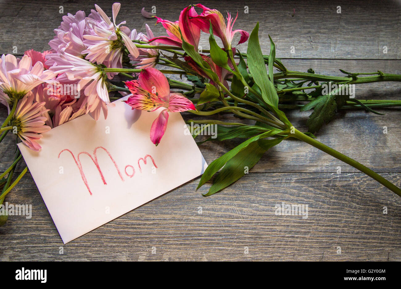 Mothers Day Bouquet And Card. Fresh bouquet of daisy, iris and carnations with a handwritten card labeled Mom. Shot from above o Stock Photo