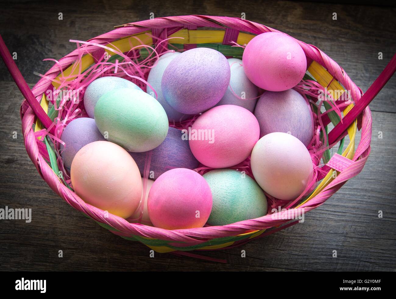 Easter Basket Background. Colorful easter eggs in a basket with grass sitting on a table. Stock Photo