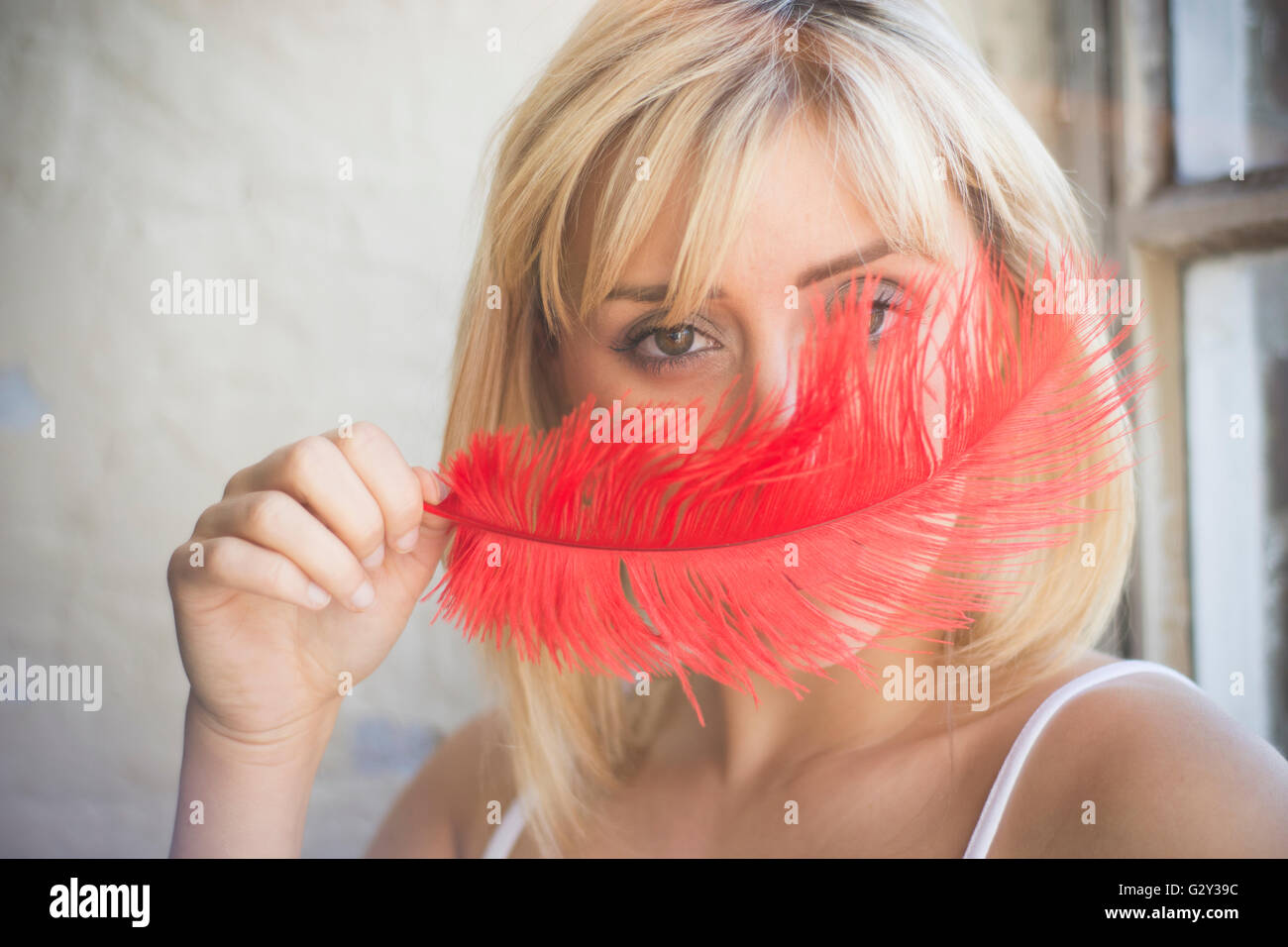 Young woman hiding face with a red feather Stock Photo - Alamy