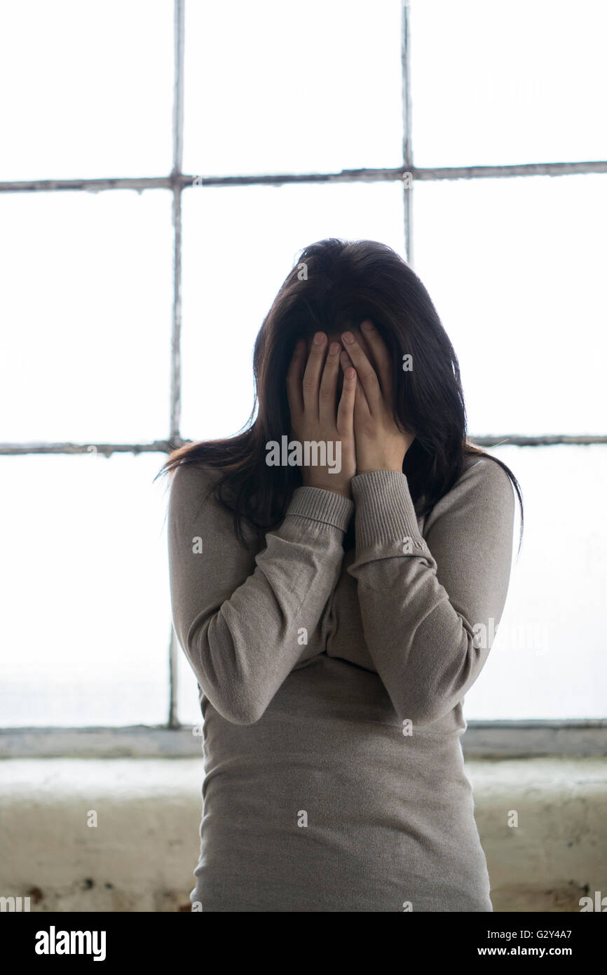 Young woman hiding face with hands by the window Stock Photo
