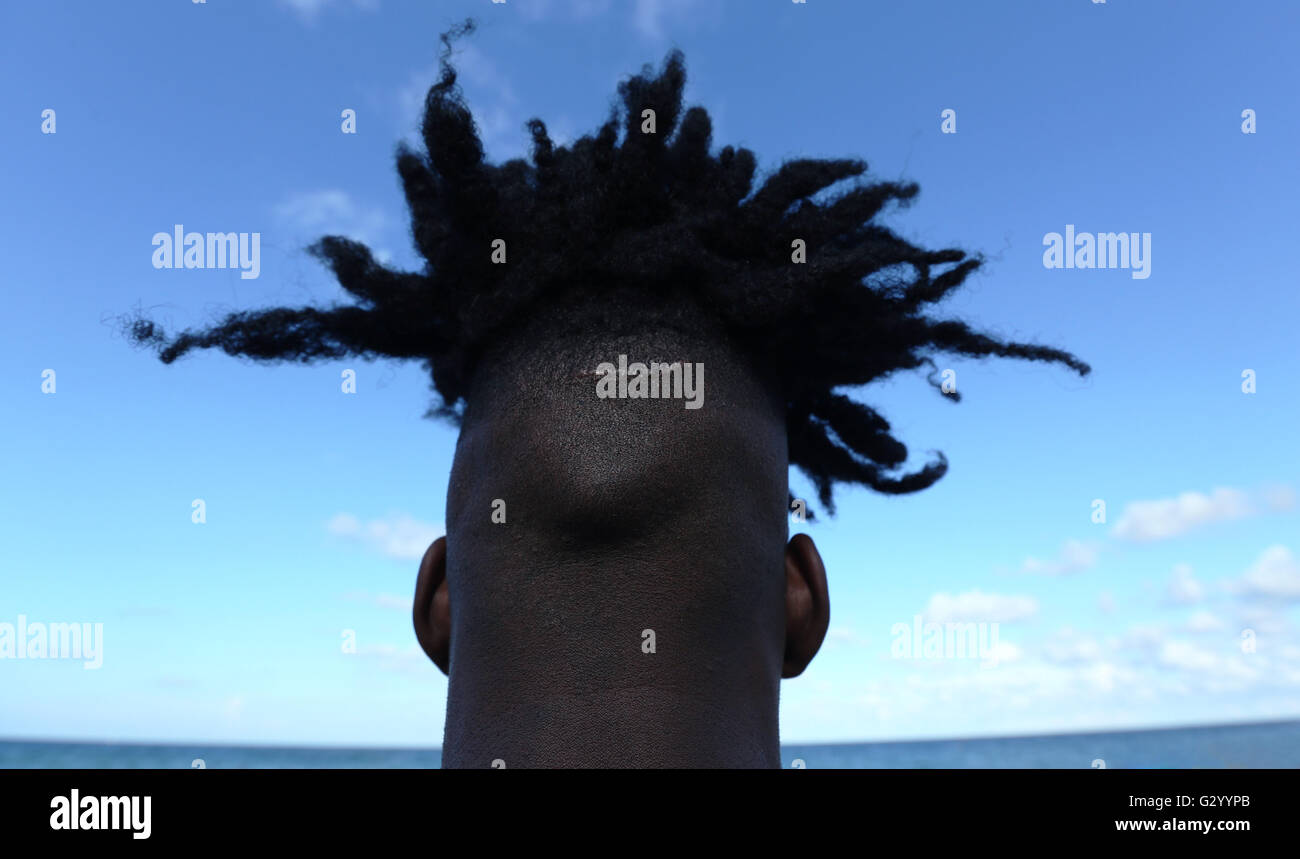 Back of head of a young African man who is facing ocean and blue sky. Stock Photo