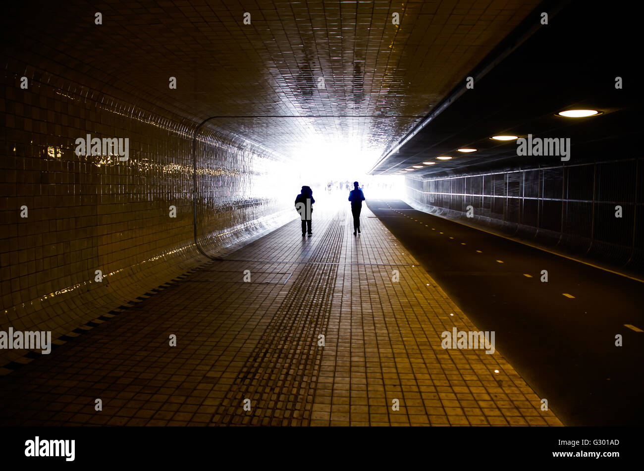 Two shadows walking in a dark empty tunnel towards bright light (Amsterdam train station tunnel, 2016) Stock Photo