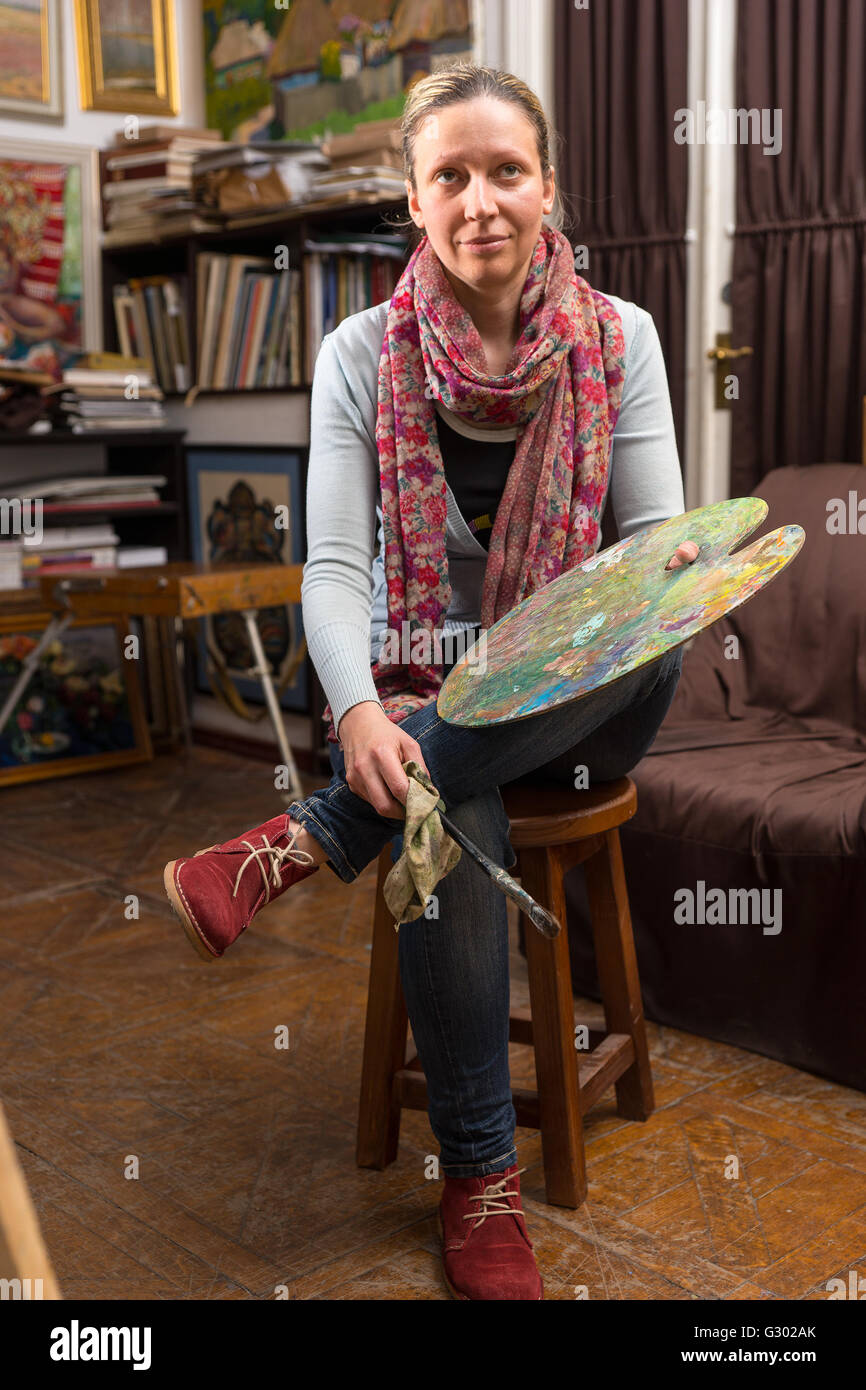 Attractive thoughtful female artist sitting painting in a studioor ...