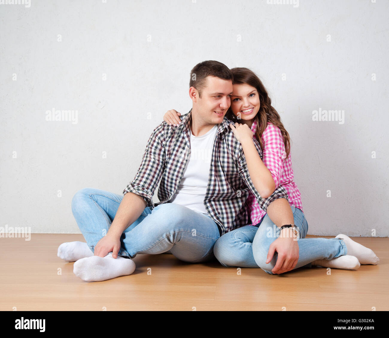 Portrait Of Happy Young Couple Sitting On Floor Looking Up Ready for ...