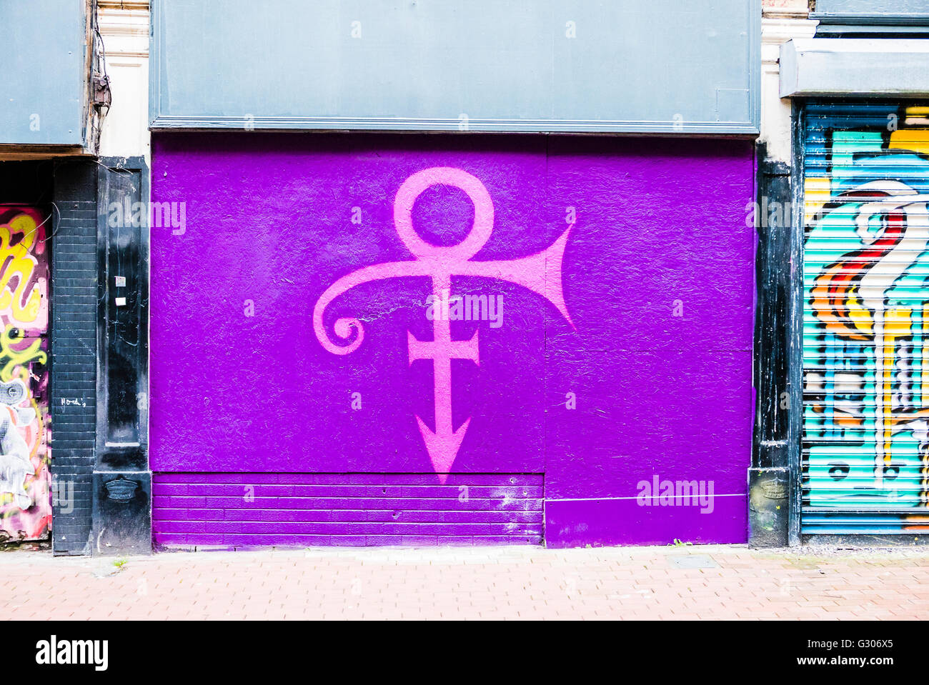 A tribute is painted on the front of a closed-down shop to the singer Prince who died in 2016, of his 'Symbol' on a purple backg Stock Photo