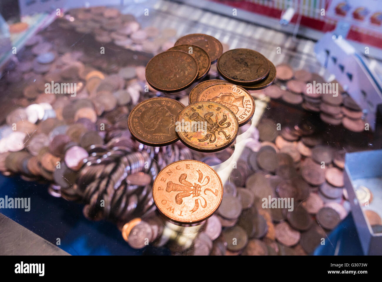 Two-pence coins lie on the glass on top of a 2p nudger machine in a seaside amusement arcade. Stock Photo