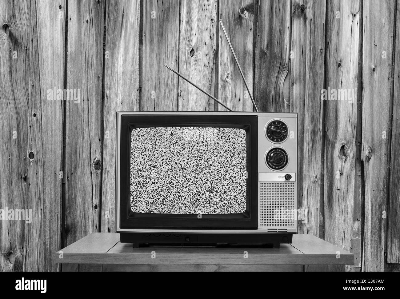 Vintage television with rustic wood wall and static screen in black and white. Stock Photo