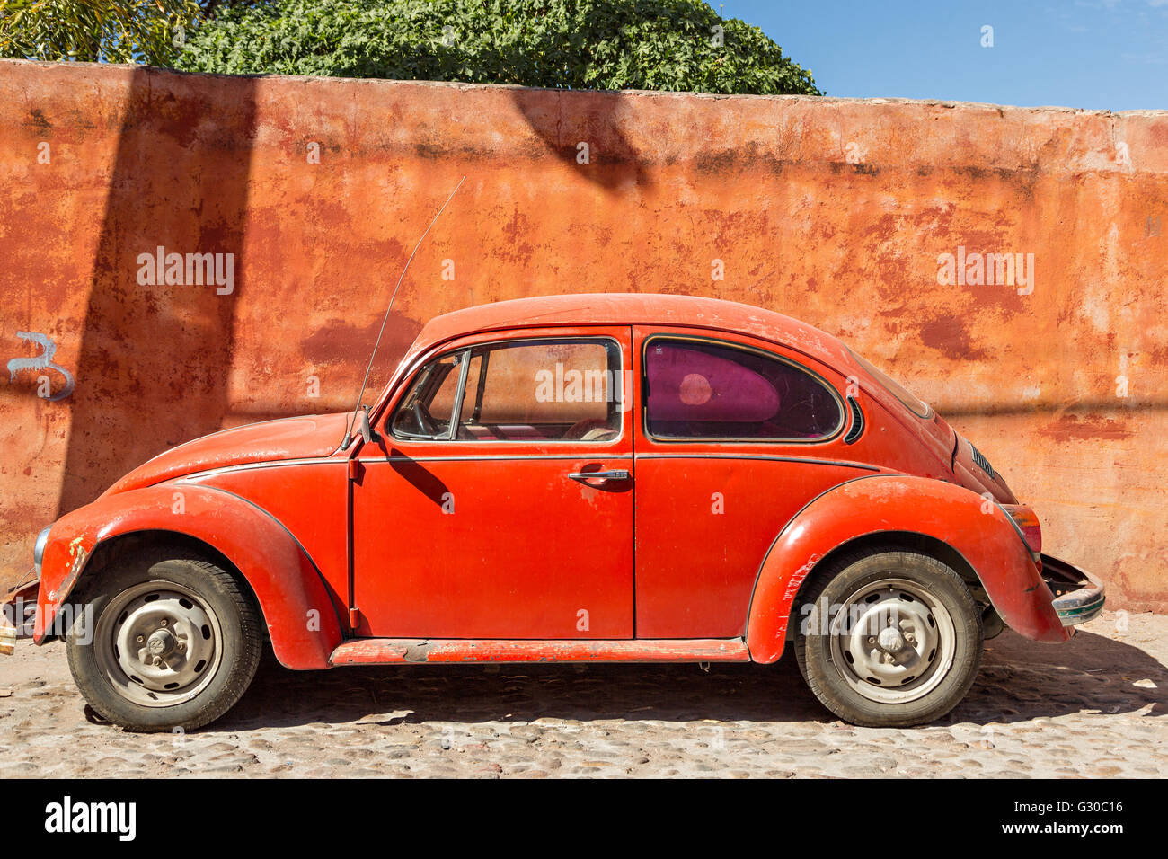 An old red Volkswagen Beetle car parked against a red wall in the historic center of San Miguel de Allende, Mexico. Stock Photo