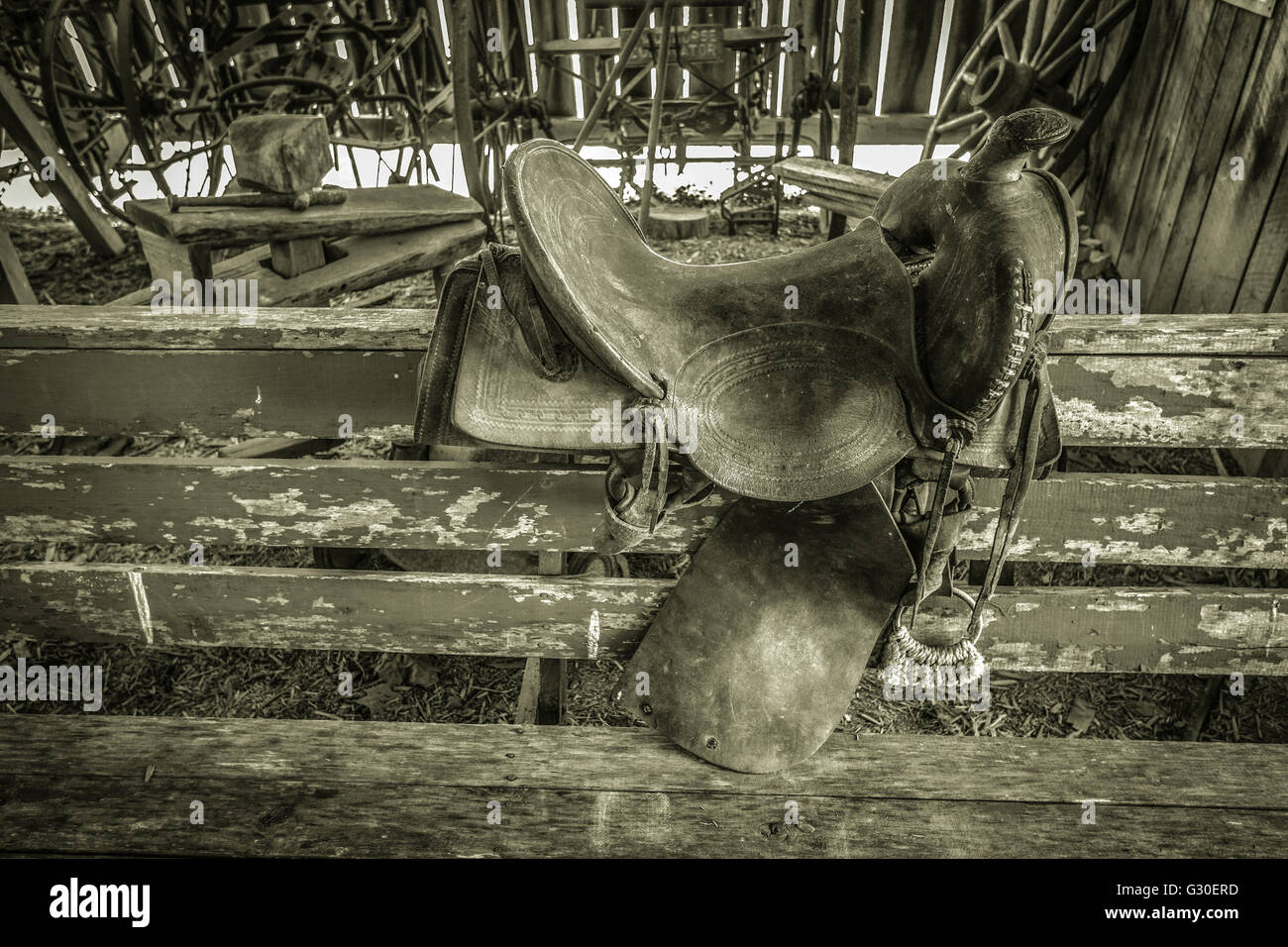 Antique Western Saddle. Black and white interior of a barn and saddle on the fence. Stock Photo