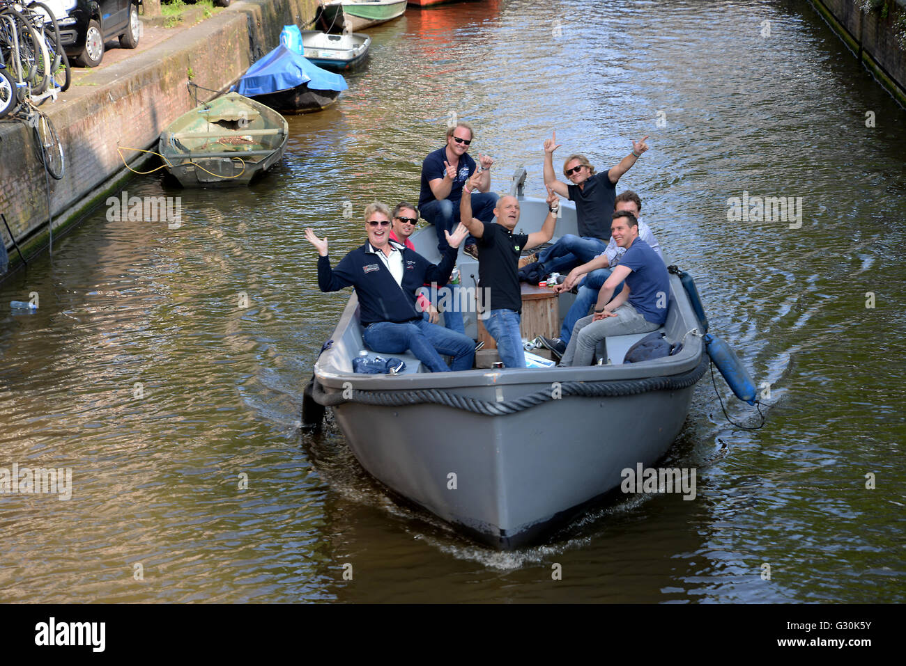Young adults laughing waving steer small open canal boat look up laugh pose photo. Stock Photo