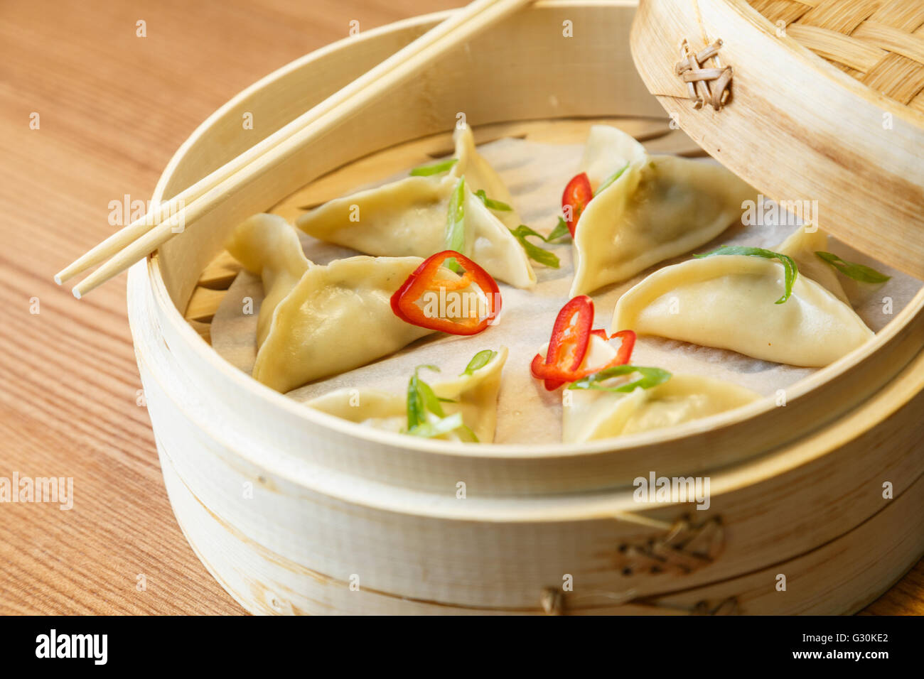 Dim sums - wontons -with a chicken meat  in a bamboo box on wooden table in asian restaurant Stock Photo