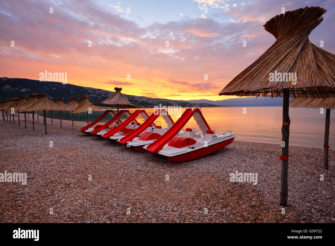 Straw umbrellas and water pedal boats on the beach in Baska, island Krk Stock Photo