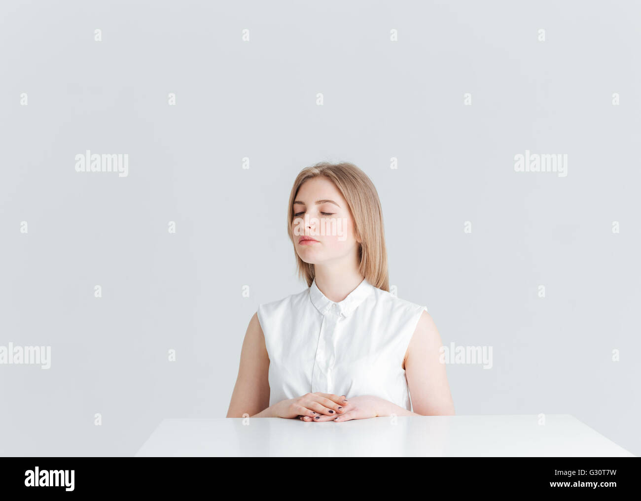 Young relaxed woman with closed eyes sitting at the table isolated on a ...