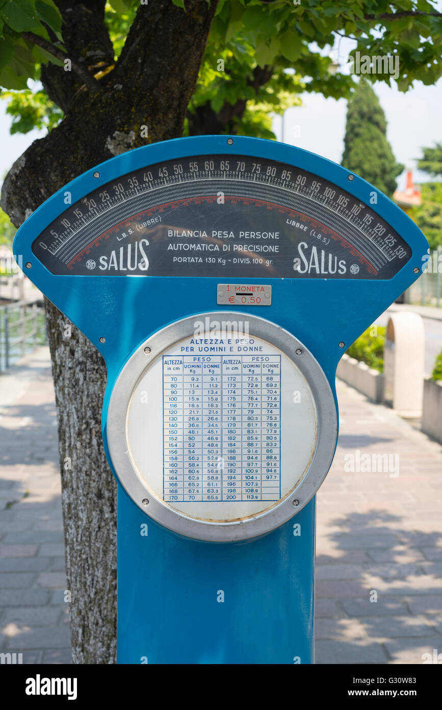 Blue weighing scale under trees on the sidewalk of the lakeside boulevard in Iseo on Lake Iseo, Lombardy, Italy Stock Photo