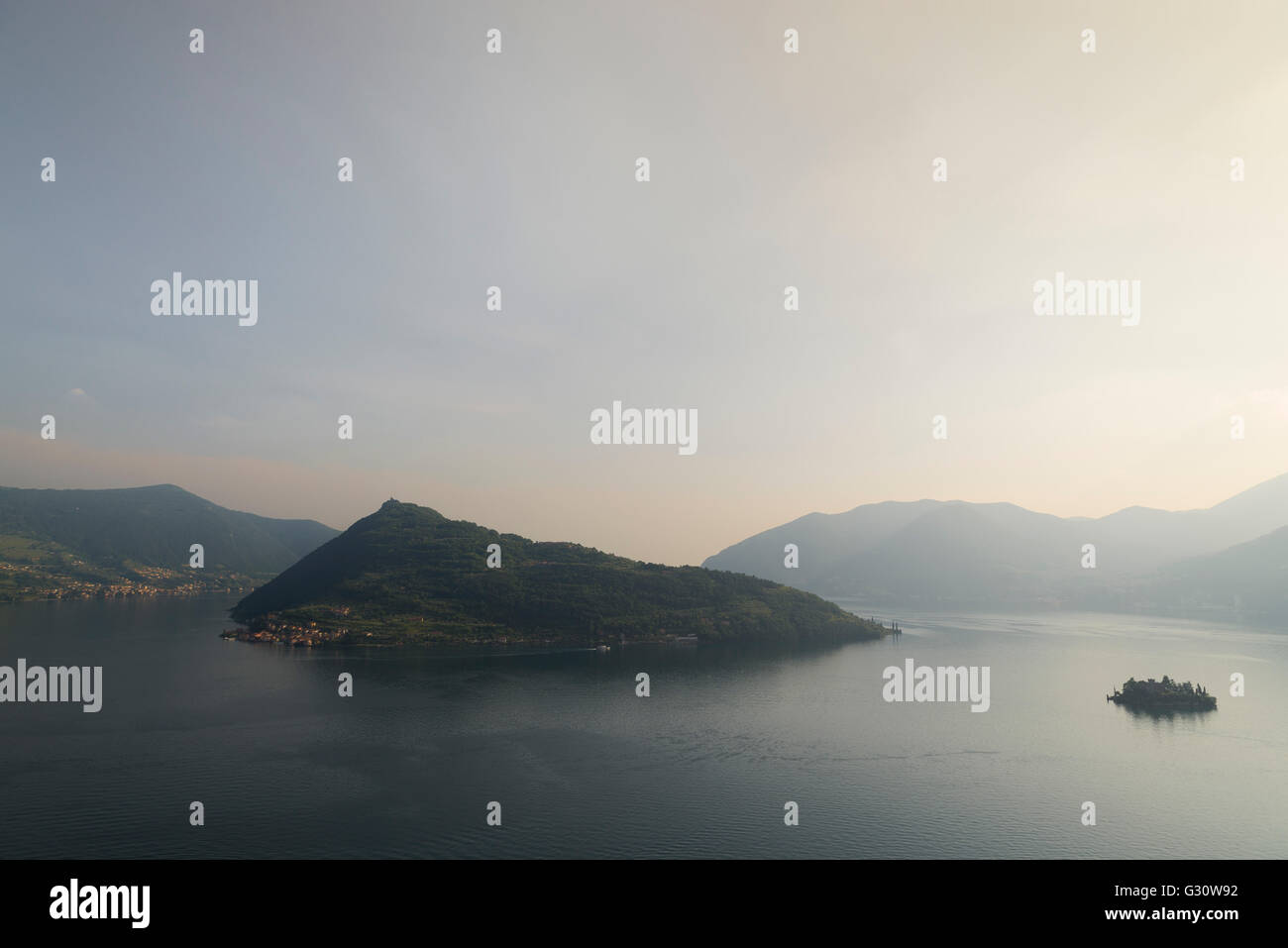 The islands of Monte Isola and Isola di Loreto at Lake Iseo with surrounding mountains and a glowing sky at sunset Stock Photo