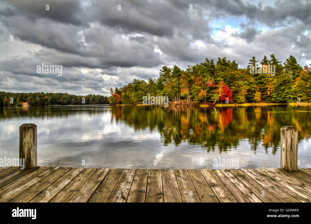 An Autumn Day At The Lake. Wooden dock overlooking a lake and an island ablaze in fall splendor. Ludington State Park. Ludington Stock Photo