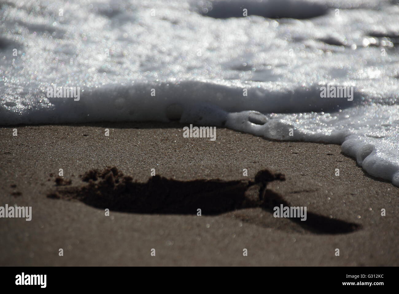 footstep on sandy beach, approached by wave Stock Photo