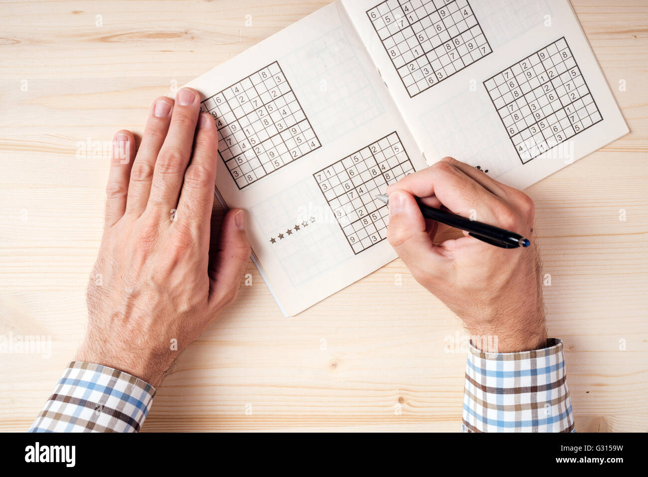 Top view of male hands solving sudoku puzzle on wooden office desk Stock Photo