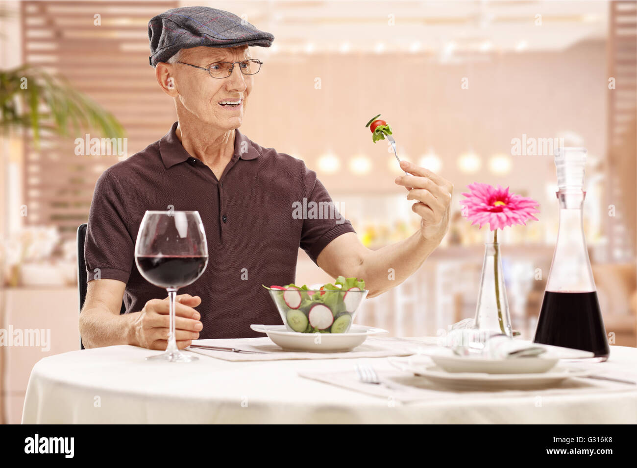 Discontent mature man sitting in a restaurant and looking at their food in disgust Stock Photo