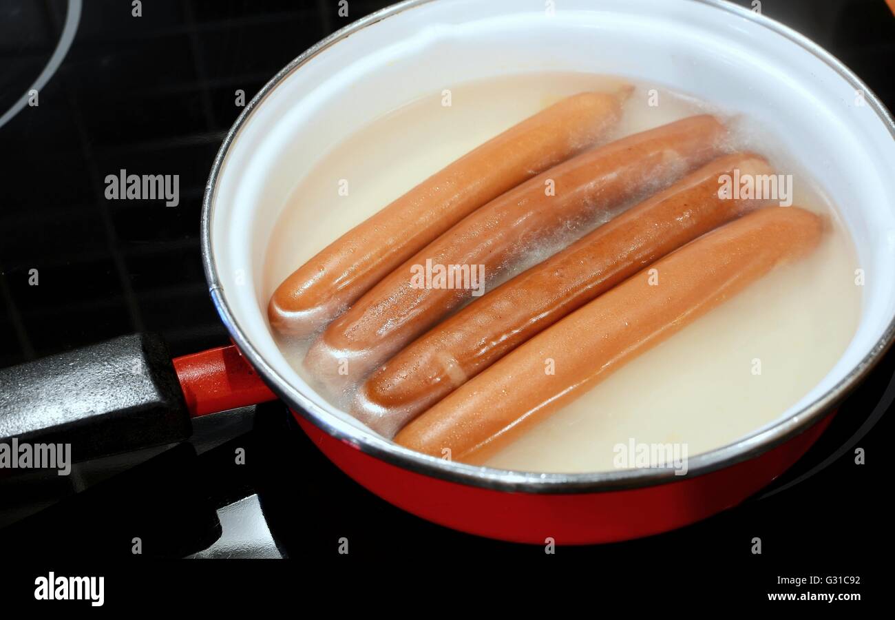 Four sausages (frankfurter wurst) boiling in hot water in pan. Boiling frankfurter sausages. Stock Photo