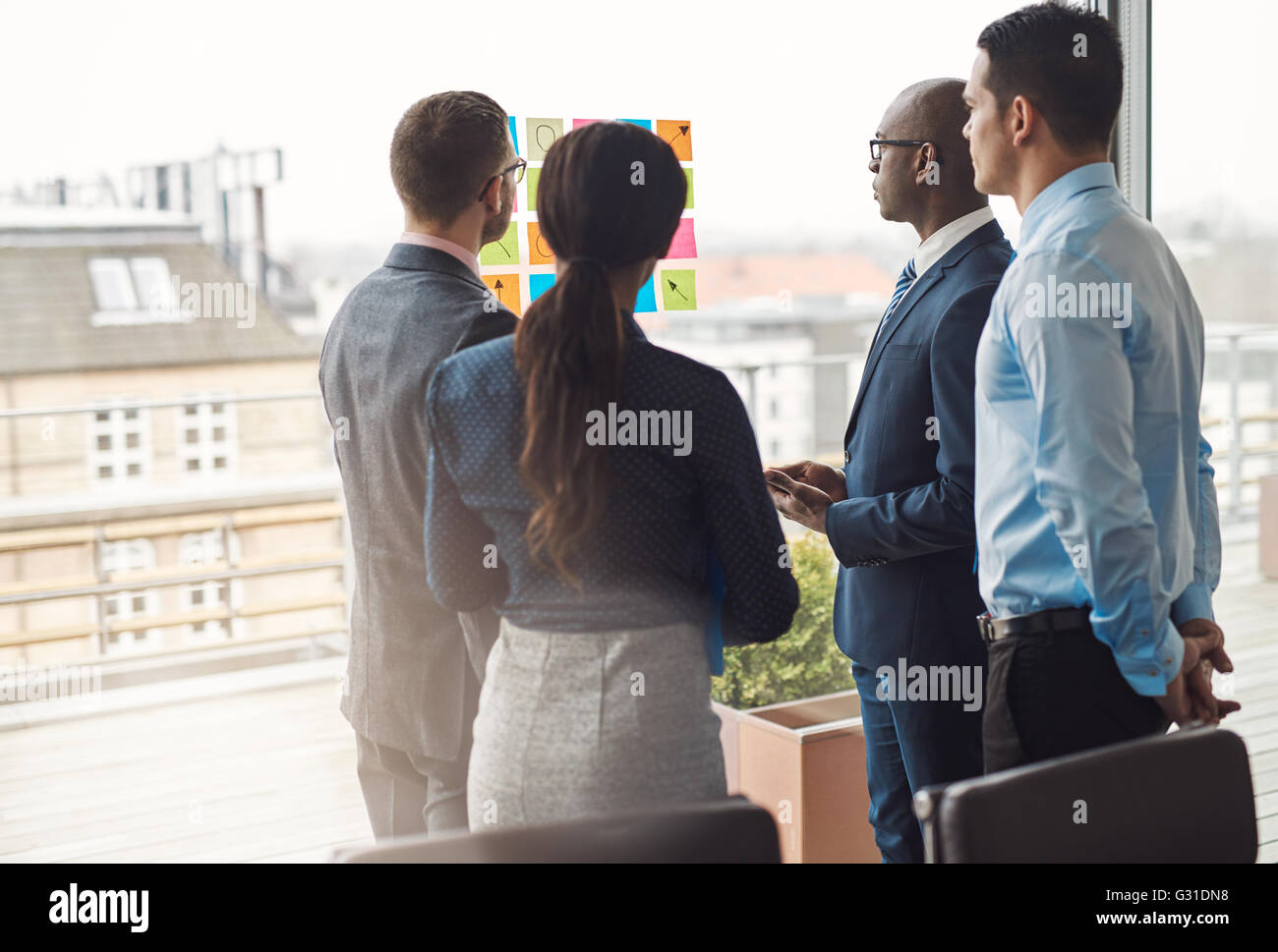 Four diverse multiracial businesspeople standing in a group in front of a high key window looking at a set of colorful memos stu Stock Photo