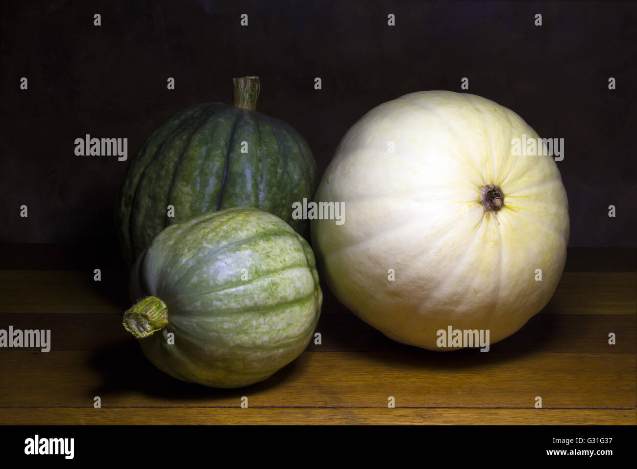 Three pumpkins still life on rustic wood table semi lit ambiance Stock ...