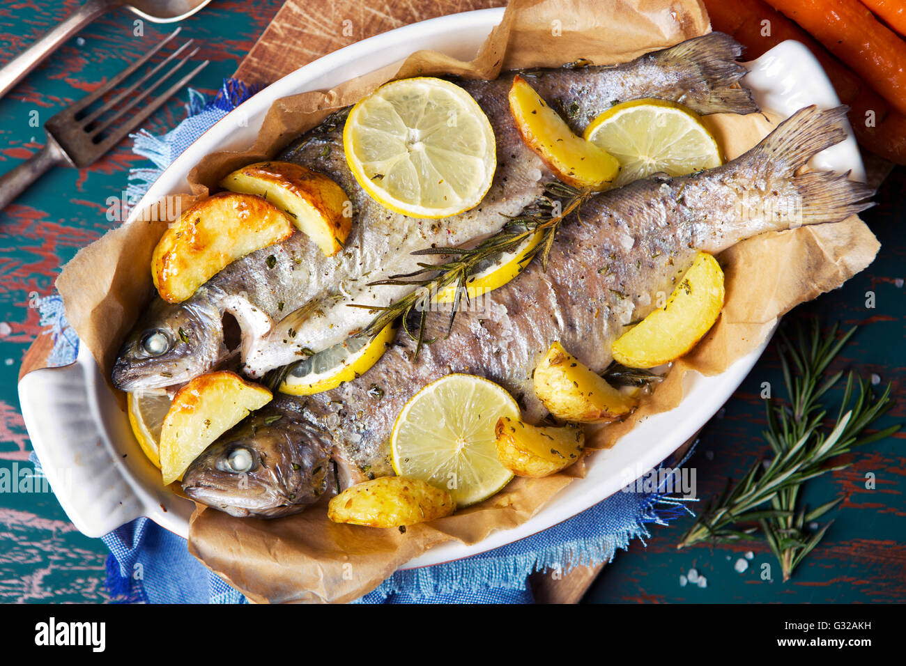 An oven roasted trout in a casserole on a rustic table. With carrots
