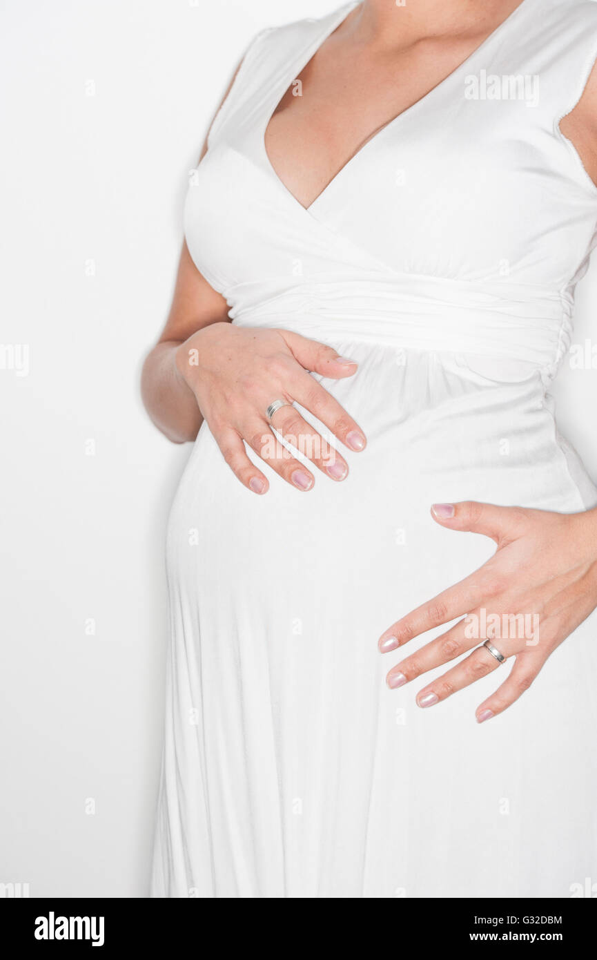 Pregnant woman in a white dress holding her hands on her belly Stock ...