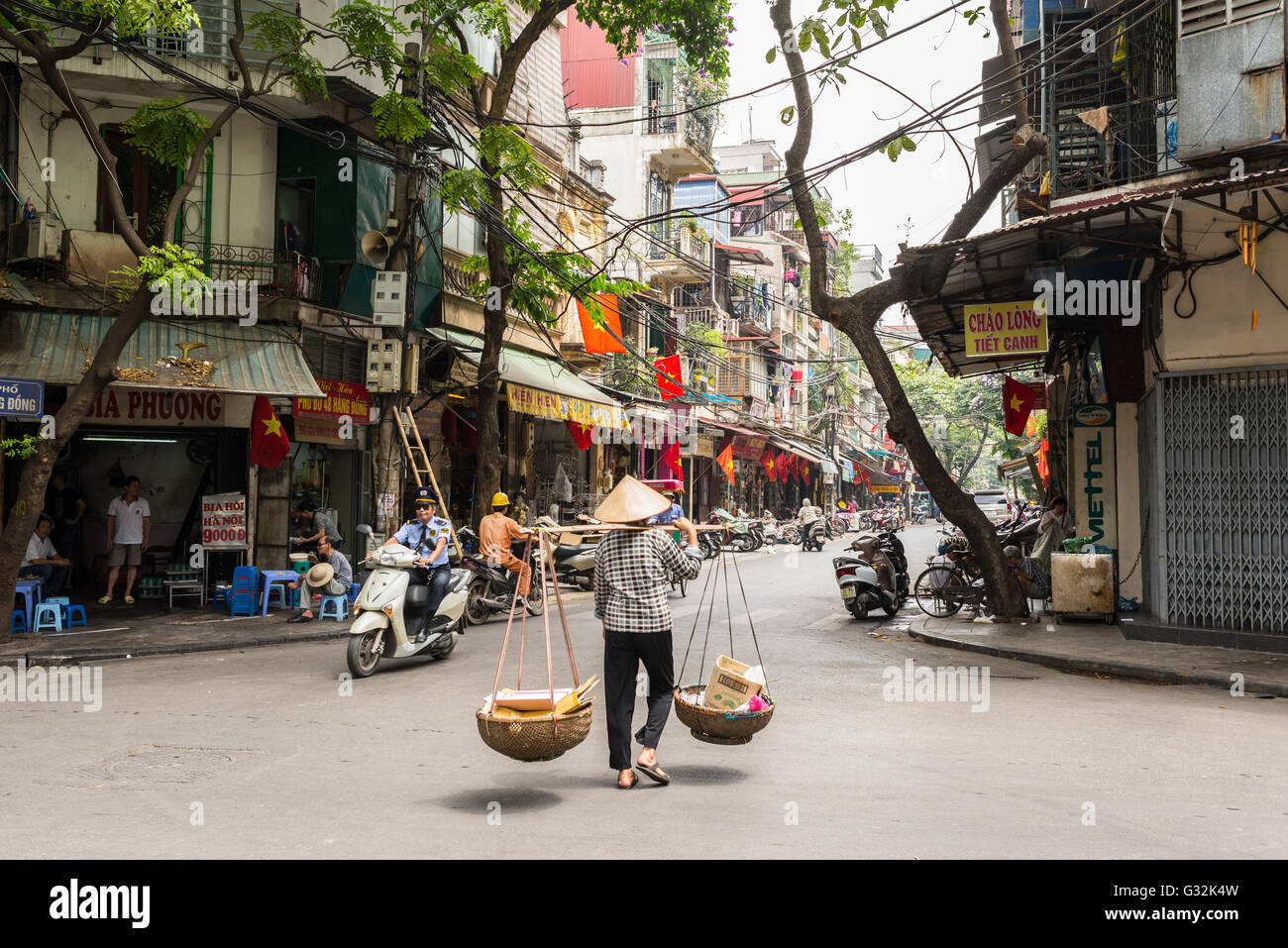 Street vendor transporting goods in baskets using a carrying pole in Hanoi's Old Quarter. Stock Photo