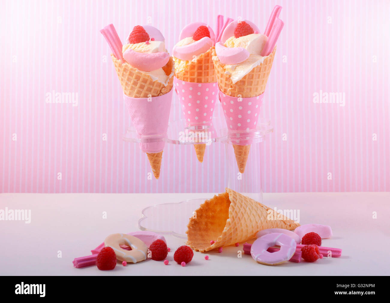 Summer is Here themed vanilla ice creams in wafer cones with pink candy decorations on a white wood table against a pink stripe  Stock Photo