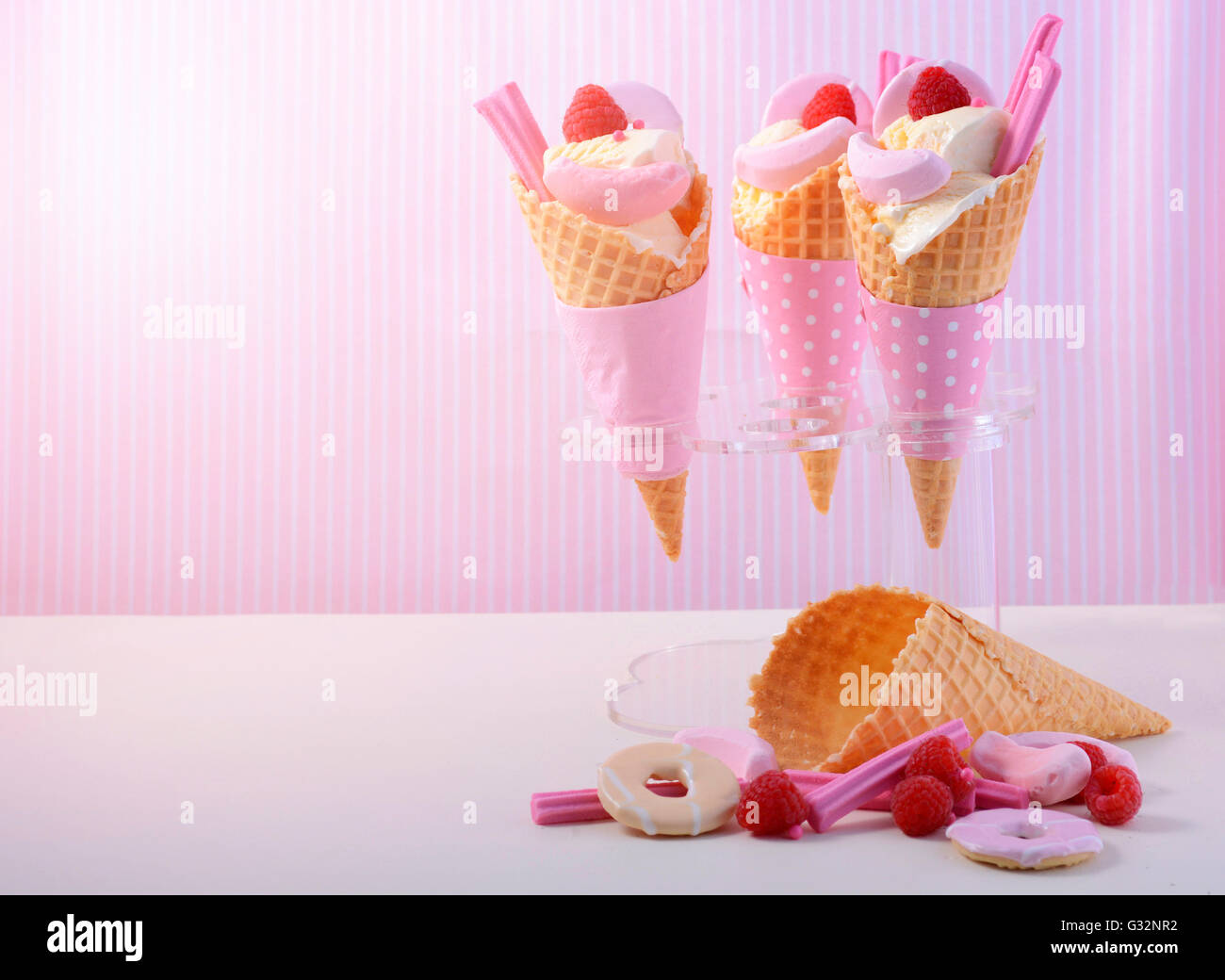Summer is Here themed vanilla ice creams in wafer cones with pink candy decorations on a white wood table against a pink stripe  Stock Photo