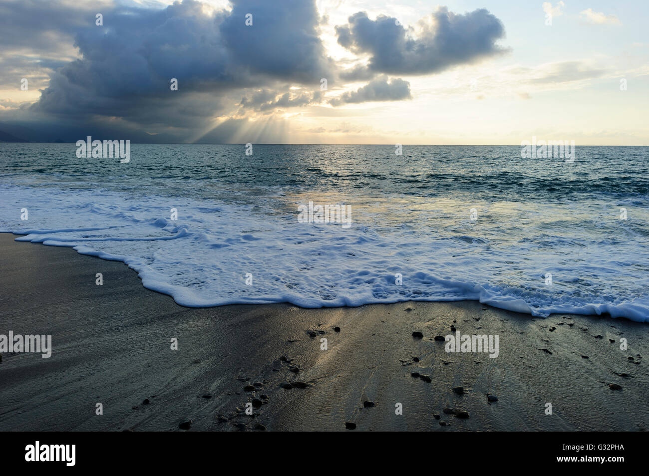 Ocean sunset sun rays is an ominous storm moving in over the ocean as a bright set of sunrays burst through the darkness to ligh Stock Photo