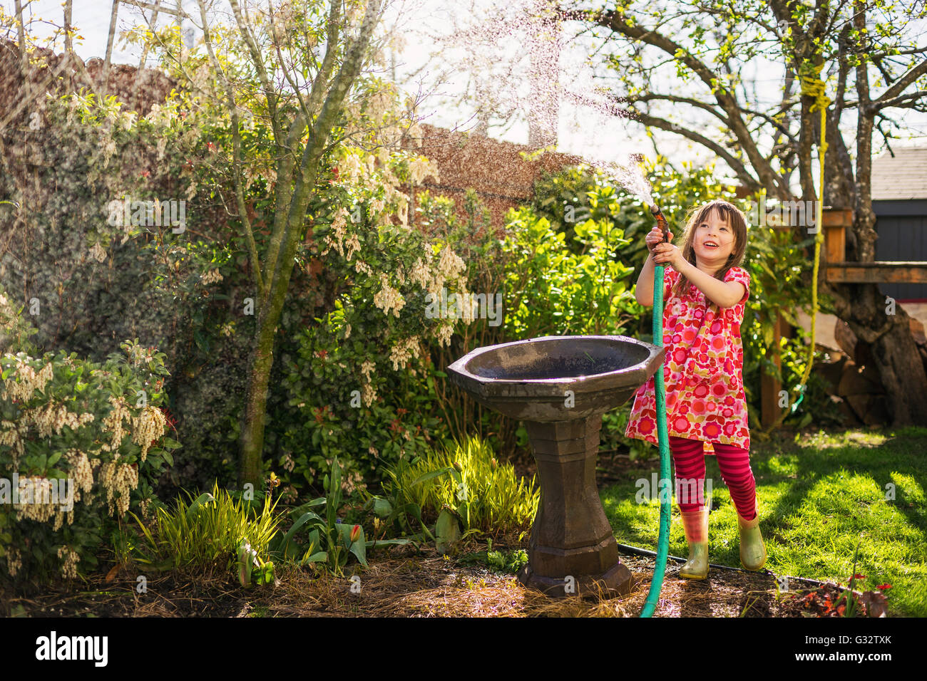 Girl watering plants in garden with hosepipe Stock Photo