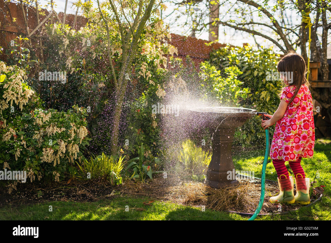 Girl watering plants in garden with hosepipe Stock Photo