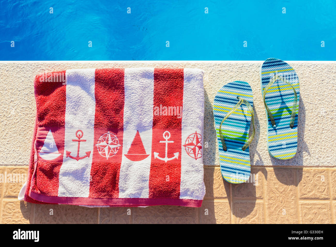 Bathing slippers and bath towel at blue swimming pool in summer Stock Photo