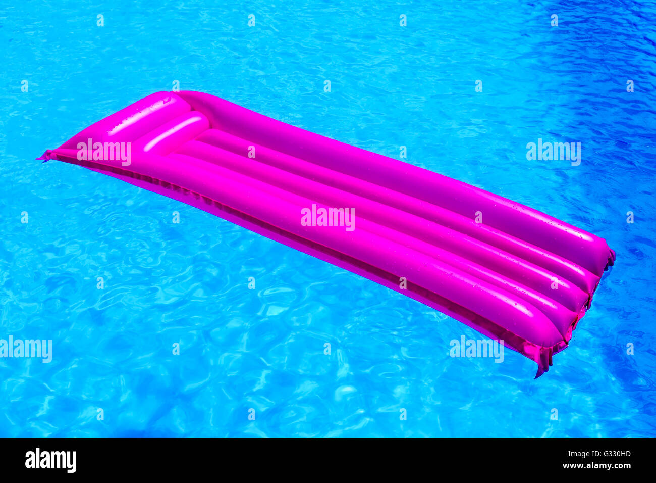 Pink air mattress floating on water of blue swimming pool Stock Photo