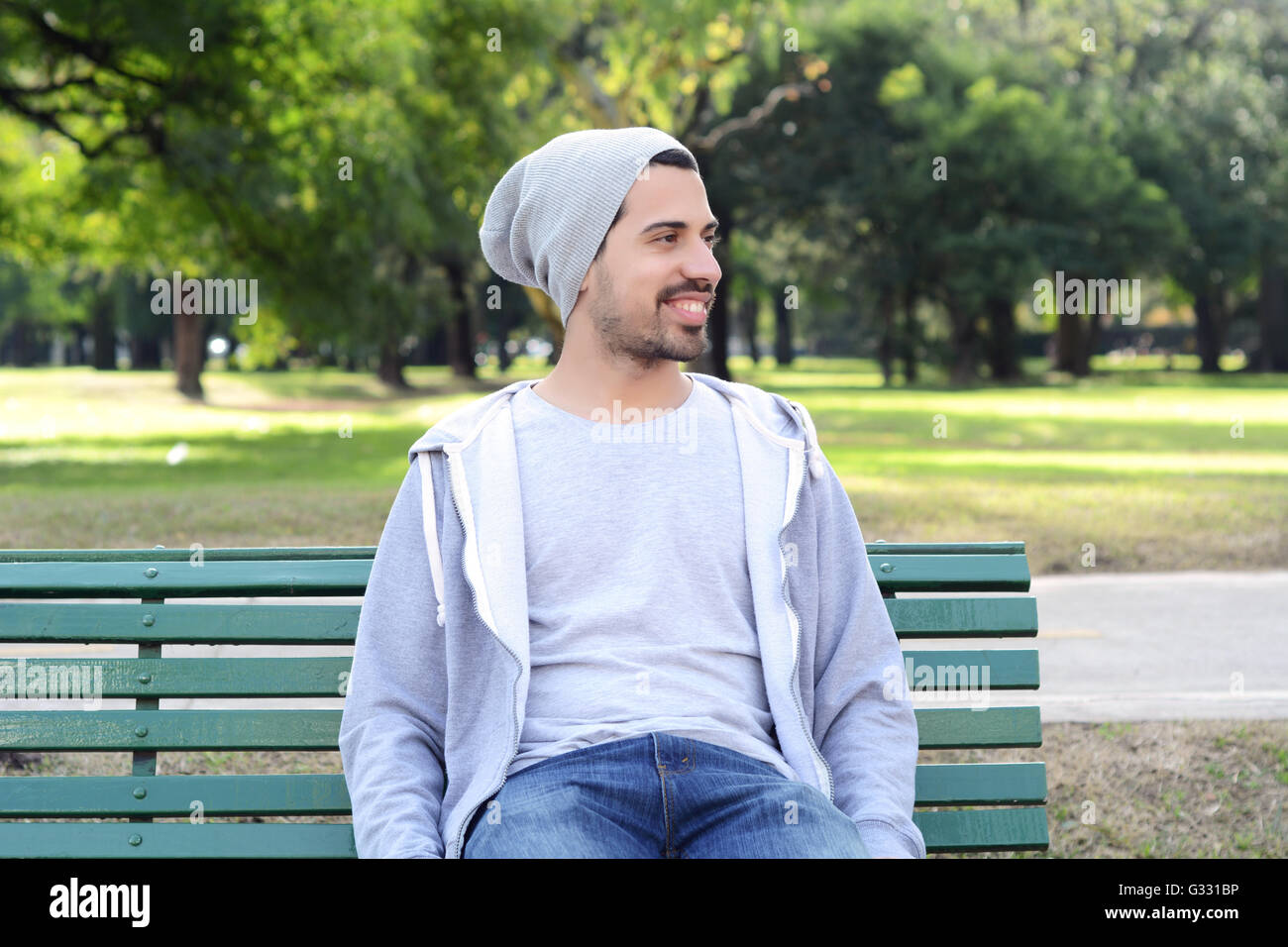 Portrait of young latin man sitting on park bench. Outdoors Stock Photo