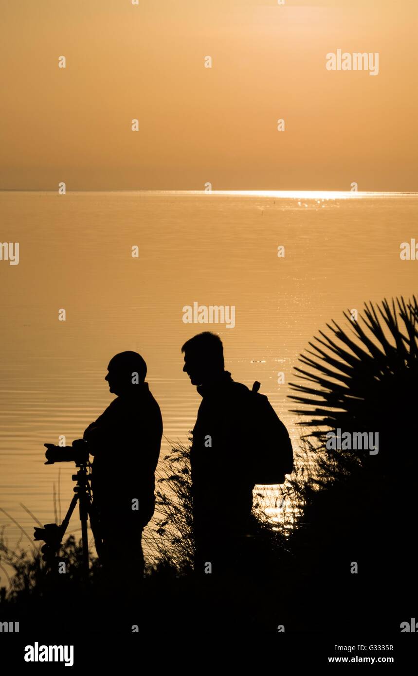 silhouette of two men on silhouette at sunset by the sea Stock Photo