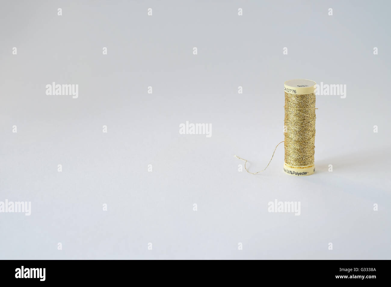 Spool of shiny gold thread isolated on a white background with copy space to the left. Stock Photo