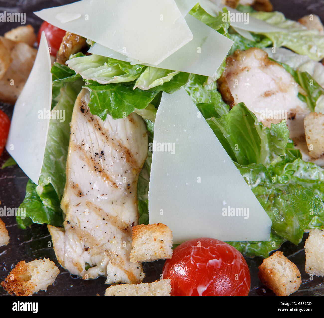 Macro fragment of salad with grilled chicken meat, lettuce, tomatoes and croutons.  Glass dish on a brown wooden Stock Photo