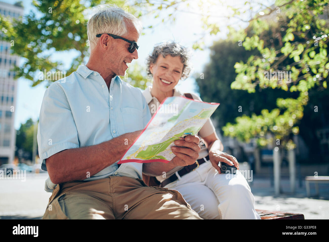 Senior tourist sitting on a bench and looking for a place on the map. Relaxed mature couple on a holiday, using a map for findin Stock Photo