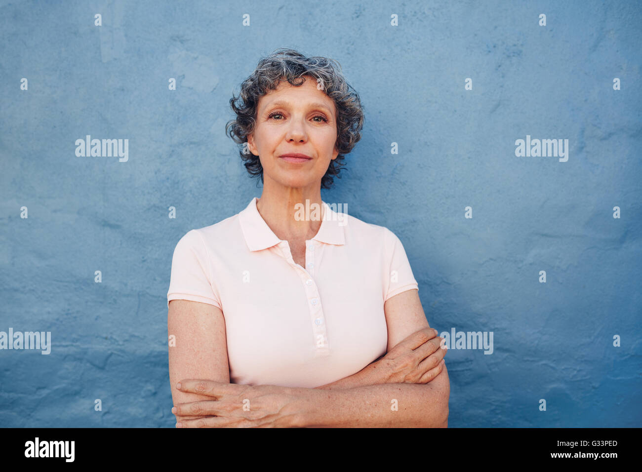 Portrait of confident mature woman standing with her arms crossed against blue background Stock Photo