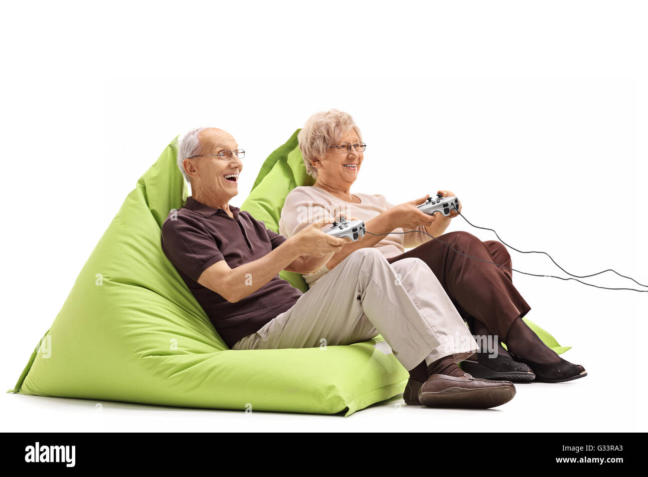 Elderly couple playing video games seated on green beanbags isolated on white background Stock Photo